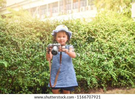Little girl child photographing - cute child holding photo camera in the garden park / young girl taking photos by digital camera