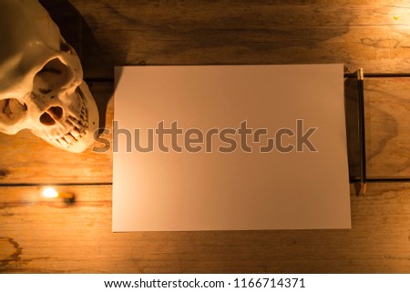 Human skull with candle light and white paper with pencil on wooden table, Decorated for Halloween Theme with copy space.