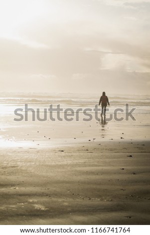 A woman walking towards the ocean exploring the nature in Tofino, British Columbia, Canada. A local beach welcomes her with cold and sunny weather during a beautiful sunset.