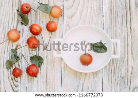 Wild, ripe red apples with leaves in earthenware on a light wooden background.