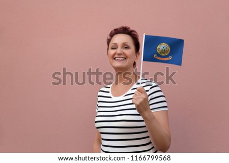 Idaho flag. Woman holding Idaho state flag. Nice portrait of middle aged lady 40 50 years old with a state flag over pink wall on the street outdoors.