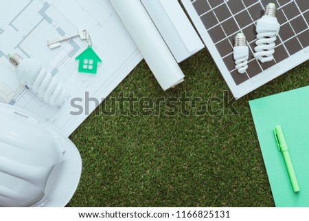 Sustainable green building and energy saving concept: house project, solar panel and work tools on the grass, top view Royalty-Free Stock Photo #1166825131