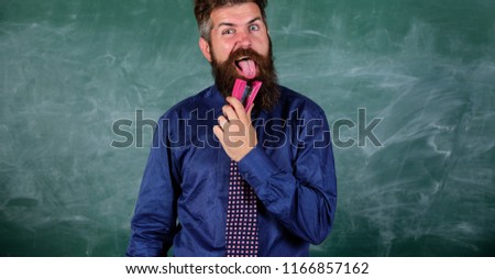 School stationery. Teacher bearded man with pink stapler chalkboard background. School accident prevention. Hipster teacher formal wear necktie holds stapler. Man scruffy use stapler dangerous way.