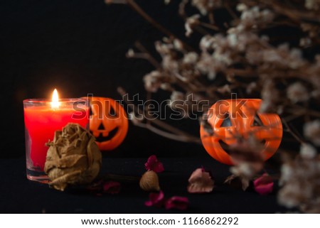 Orange pumpkin as a head with carved eyes and a smile with burning candles on a black background, Halloween home decoration