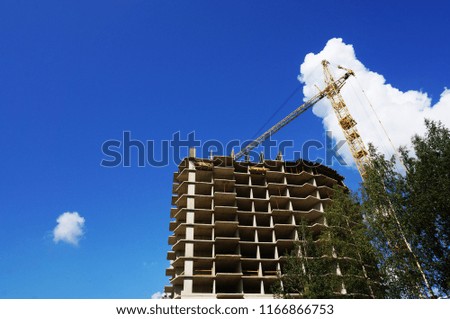  The basis of a house under construction, a working tower crane against the blue sky in summer weather.  