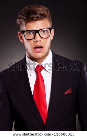 closeup picture of a young business man acting surprised with his mouth opened, against dark background