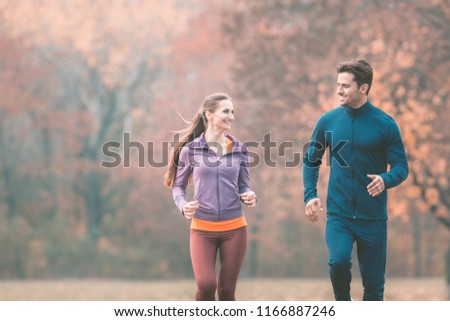 Couple in wonderful fall landscape running for better fitness towards the camera