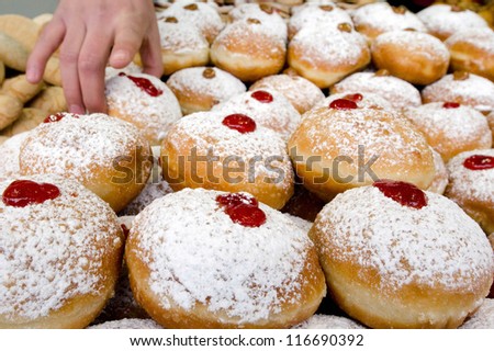 Jewish person hand picking up a fresh Hanukkah Doughnut from a bakery stall display in Jerusalem market on the Jewish Holiday of Chanukah.