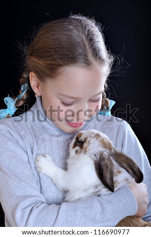 Studio portrait of a girl and a rabbit. The child looks at the animal
