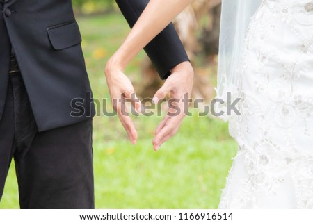 Beautiful Bride on wedding dress and groom with suit has love permission and express with  the sign of heart shape by hands on wedding day / wedding couple concept 