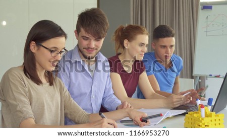Young caucasian people working in pairs at the office. Handsome brunette guy in blue t-shirt explaining something on laptop to female redhead coworker. Attractive bearded man advising pretty brunette