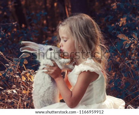 Little girl in white dress play with rabbit.