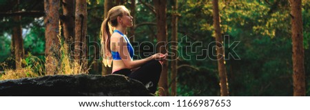 Blonde woman doing exercises outdoors on a rock in the forest. Yoga nature concept