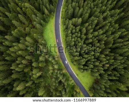 Aerial view of road and  cars passing by in green forest in mountains. drone shot