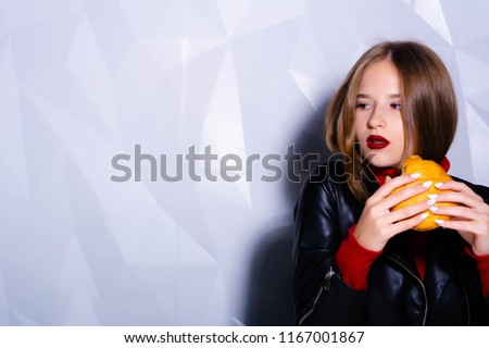 Young beautiful slender girl holds a burger in her hands and looks at him and licks herself. The concept of an unhealthy diet. Fast food. Diet. Junk food. Food. Burger