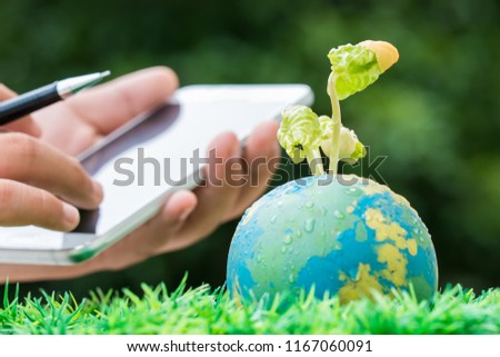 Student Hand holding smartphone for studying or researching seeding plant on Globe model in outdoor lab on sunny  green grass, Green save world environment ecology day, Life on earth concept
