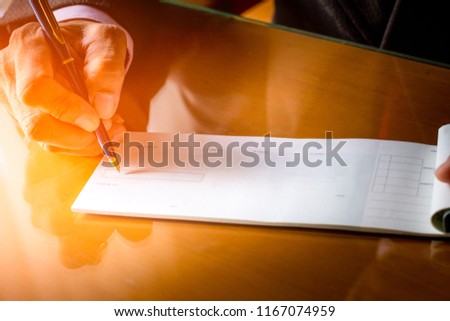 Business man hand writing and signing checkbook on the wooden table background at office. Paycheck or payment by cheque concept. Royalty-Free Stock Photo #1167074959
