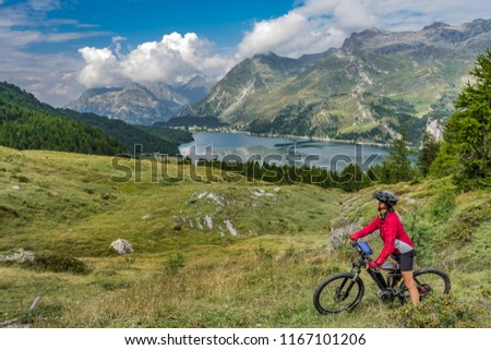 Senior woman, riding here e-mountain bike on the famous trails around the lakes in the upper Engadin, between Saint Moritz and Maloja, Engadin, Switzerland with stunning views on the lake of Silvaplan