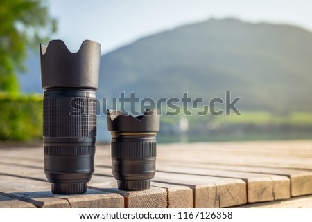 Zoom lens and lens with fixed focal length from digital camera standing on wooden board with mountain landscape at background Royalty-Free Stock Photo #1167126358