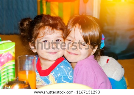 Joyful beautiful 5 year female child hugging tight her sister, both sitting at the dinner table and smiling. Together forever