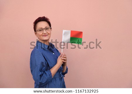 Madagascar flag. Woman holding Madagascar flag. Nice portrait of middle aged lady 40 50 years old with a national flag over pink wall background outdoors.