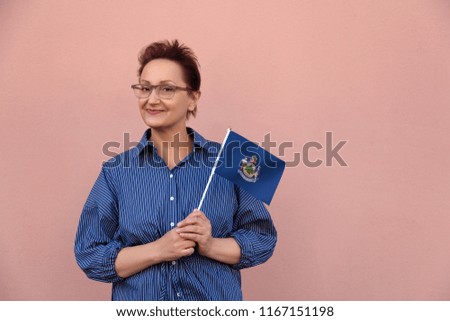 Maine flag. Woman holding Maine state flag. Nice portrait of middle aged lady 40 50 years old with a state flag over pink wall on the street outdoors.