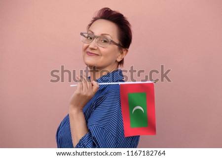 Maldives flag. Woman holding Maldives flag. Nice portrait of middle aged lady 40 50 years old with a national flag over pink wall background outdoors.
