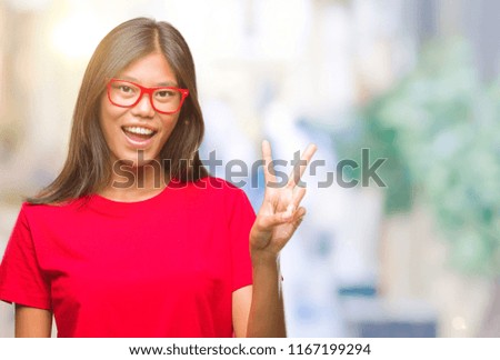 Young asian woman wearing glasses over isolated background smiling with happy face winking at the camera doing victory sign. Number two.