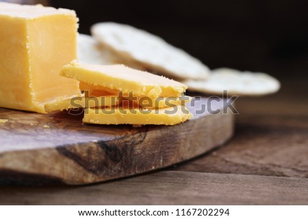 Block of cheddar cheese and slices over a rustic background.. Extreme shallow depth of field with selective focus on cheese. Water crackers in the background.  