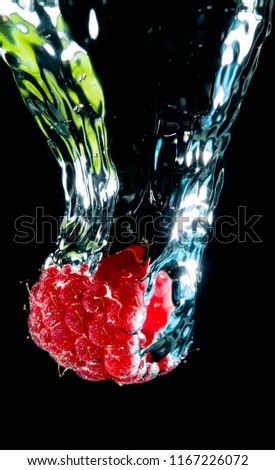 Closeup shot of ripe raspberry covered with air bubbles and falling down in water on black background