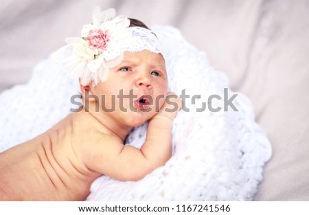 A sweet Caucasian newborn baby girl with a surprised look on a white pillow with flower hair bow on her head. A cute two week old infant portrait.