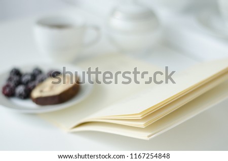 Morning table with cup of tea,biscuit slice and book. Selective focus on book pages.