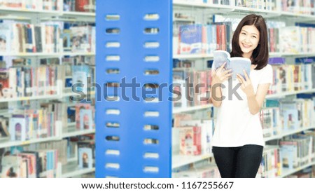 Young asian woman reading a book at bookshelf in library.student girl holding book on hand and celebrating while standing in the library