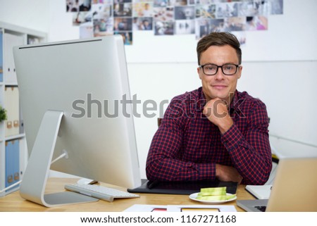 Portrait of cheerful web designer sitting at office table with apple slices on plate in front of him