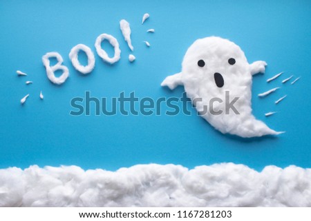 Animated ghost figure made of cotton wool flying on a blue paper background and cotton wool clouds, with black eyes and mouth. The animated text BOO!  apeears on top made of white cotton wool. 
