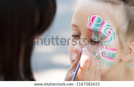 Baby face painting. Woman artist painting face of kid outdoors, copy space Royalty-Free Stock Photo #1167282655