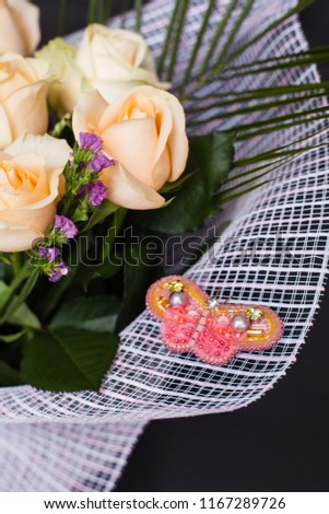 handmade accessory jewelry embroidered with beads brooches a butterfly silhouette in pink and yellow color on a a bouquet of white roses, gift