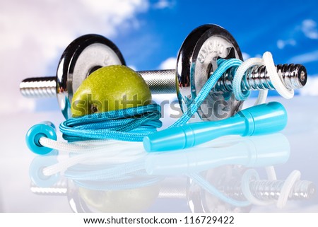 fitness dumbbells and apple on blue sky background