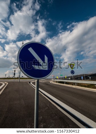 Traffic arrow sign. In the background crossroad, blue sky and white clouds.