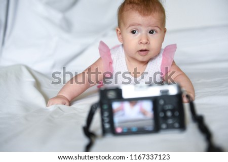 Little beautiful baby girl wondering looks at digital photo camera with her picture on the screen