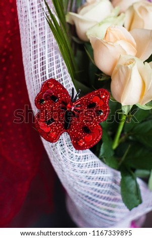 handmade accessory jewelry embroidered with beads brooches a butterfly silhouette in red color on a a bouquet of white roses, gift
