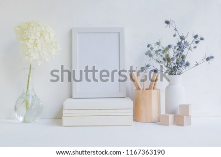 Home interior with decor elements. White frame, flowers in a vase, books and pencils