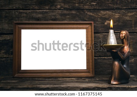 Empty photo frame and burning candle on aged wooden table background.