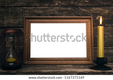 Empty photo frame, sand watch and burning candle on aged wooden table background.