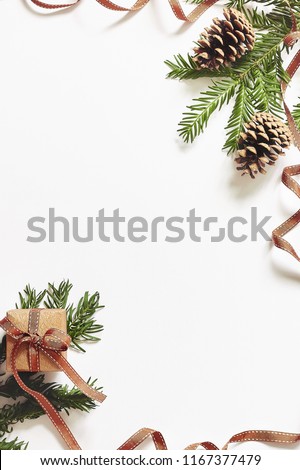Christmas and New Year composition. Gift box with ribbon and fir branches with cones on white background. Flat lay, top view, copy space for text, vertical