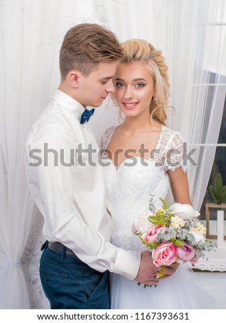 Beautiful newlyweds sitting and holding hands in a gray studio. Portrait of the bride and groom in a lace dress. A gentle wedding portrait.