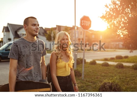 Portrait of a young couple hanging out and carrying longboard outdoors. Warm tones.
