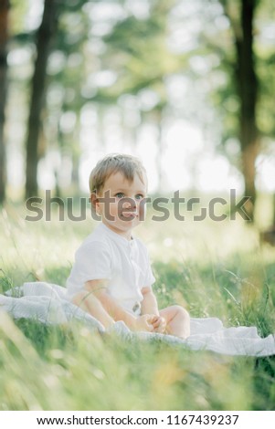 little stylish boy blond with blue eyes dressed in a white shirt posing for the photo outside