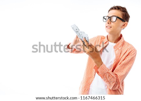 A young man with glasses throws a hundred dollars bills, a portrait of a successful teenager in a shirt in the Studio