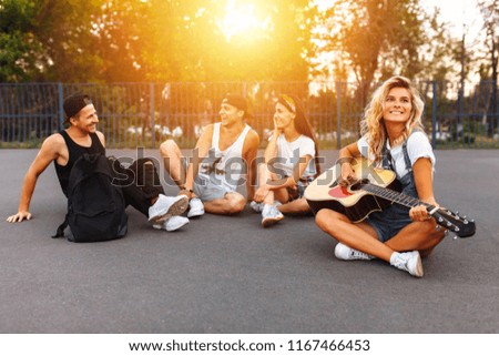 A group of friends having fun at sunset on the asphalt in a skate Park, playing guitar, good summer mood